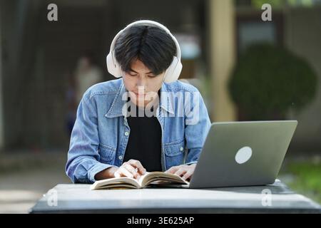 E-Learning. Glücklicher Asiatischer Mann Student Mit Tablet-Computer, Der Kopfhörer Trägt, Steht In Der Nähe Des Universitätsgebäudes Draußen Und Surft Im Internet. Mo Stockfoto