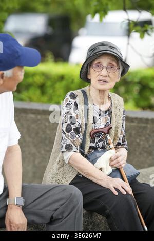 Eine ältere Frau sitzt auf einer Bank mit Stock und Handtasche. Ein Mann sitzt neben ihr Stockfoto