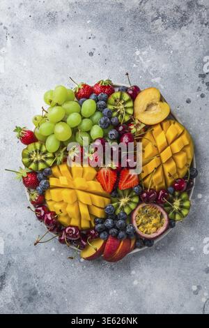 Essen, köstliche Obst- und Beerenplatte. Mango, Kiwi, Erdbeere, Traube, Kirsche, Heidelbeere, Pfirsich und Passionsfrucht, Blick von oben Stockfoto