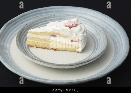 Ein kleiner japanischer Erdbeerkuchen auf zwei stilvollen überlappenden großen und kleinen Tellern im japanischen Stil auf einem schwarzen Tuch auf einem weißen Tisch Stockfoto