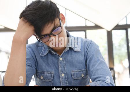 Ein junger Mann, der gestresst aussieht und den Kopf hält, während er tief nachdenkt. Sein Ausdruck zeigt Frustration oder Erschöpfung, möglicherweise mit einem Diffi umzugehen Stockfoto