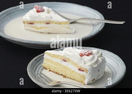 Ein kleiner japanischer Erdbeer-Shortcake und je eine Gabel auf zwei stilvollen, großen und kleinen Tellern im japanischen Stil auf einem schwarzen Tuch auf einem weißen Tisch Stockfoto