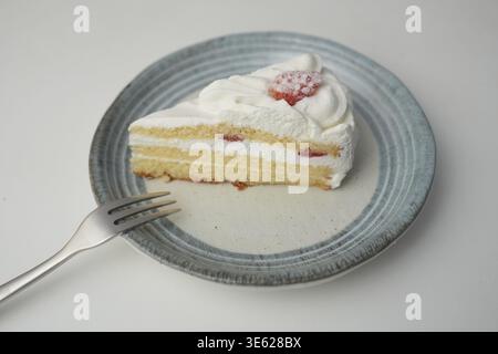 Ein kleiner japanischer Erdbeer-Shortcake und eine kleine Gabel auf einem stilvollen japanischen Teller auf einem weißen Tisch Stockfoto
