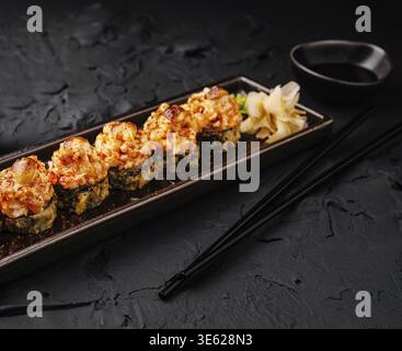 Essen, leckere Sushi-Brötchen, garniert mit gebackenen Garnelen und garniert mit eingelegtem Ingwer. Serviert in einem eleganten Restaurant mit Sojasauce auf dem Stockfoto