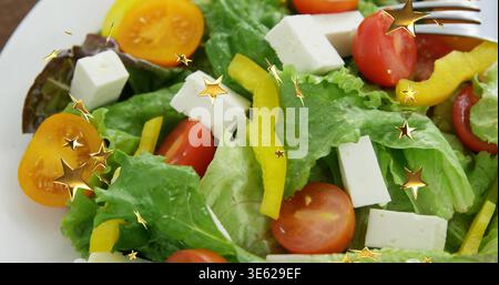 Salat auf weißem Teller auf der Tischplatte, mit Salat, Kirschtomaten, goldenen Sternen-Gabel Stockfoto