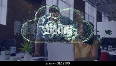 Das Team arbeitet am Laptop im Büro, eine Frau in Senfspitze, die unter holografischen Wolkengewehren schreibt Stockfoto