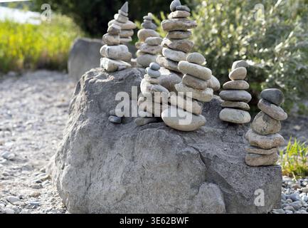 Mehrere kleine Steinstapel, die auf einem großen Felsen in einer natürlichen Umgebung im Freien ausgeglichen sind, zeigen künstlerische steinhügel umgeben von Grün und Sonnenlicht. Stockfoto