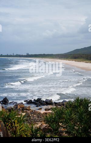 Blick aus der Vogelperspektive auf Cabarita Beach, Norries Headland, Australien ein langer Sandstrand mit sanften Meereswellen und üppigen grünen Hügeln unter bewölktem Himmel Stockfoto