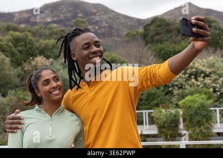 Diverse Paare, die an Deck ein Handy-Selfie machen, Mann in Senf henley, Frau in hellgrünem Reißverschluss Stockfoto