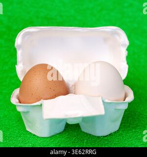 Braune und weiße frische Eier im Karton Paket auf grünem Fake Gras Hintergrund Vorderansicht Stockfoto