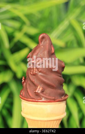 Köstlicher Schokoladeneiskegel mit weicher Portion Eiscreme gegen grünes Laub Stockfoto