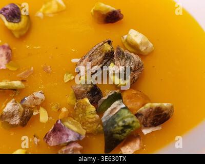 Makrofoto von einer leuchtenden Orangensuppe, wahrscheinlich Kürbis, Butternusskürbis oder Karottenbasis, serviert in einer weißen Schüssel. Das glatte, cremige Stockfoto