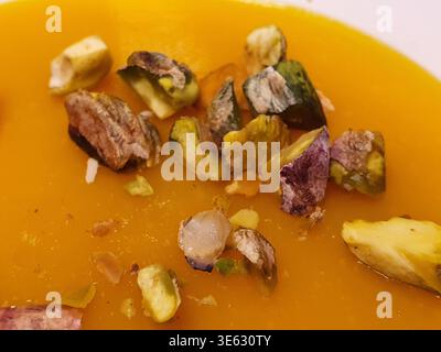 Nahaufnahme einer Schüssel mit leuchtender Orangensuppe, wahrscheinlich Kürbis, Butternusskürbis oder Süßkartoffeln, mit einer glatten, cremigen Textur. Die Stockfoto