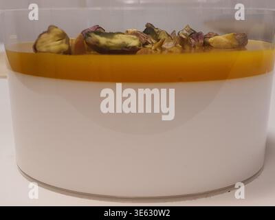 Eine Nahaufnahme eines mehrschichtigen Desserts, serviert in einem durchsichtigen zylindrischen Glasbehälter. Das Dessert besteht aus zwei unterschiedlichen Schichten: Einer dicken, undurchsichtigen Stockfoto