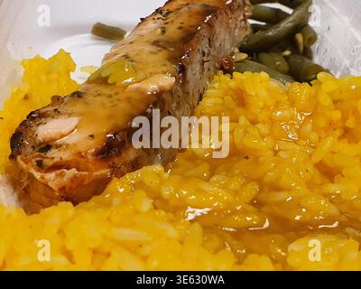 Nahaufnahme einer zubereiteten Mahlzeit, die in einem Einwegbehälter serviert wird, mit einem Stück gegrilltem Fleisch, garniert mit herzhafter Sauce und kleinem Stockfoto