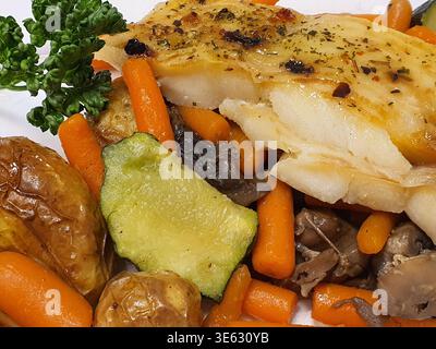 Nahaufnahme eines Gourmet-Menüs mit einem gewürzten Weißfischfilet mit goldbrauner Kräuterkruste, serviert auf einem farbenfrohen Medley von Stockfoto