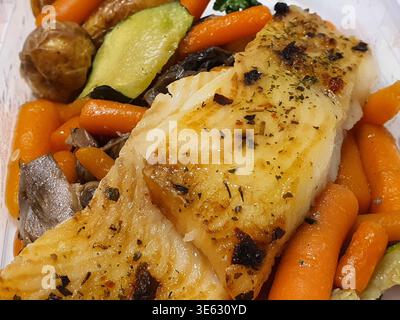 Ein Nahaufnahme einer zubereiteten Mahlzeit mit zwei gewürzten Weißfischfilets mit goldbraunen, knusprigen Oberflächen, garniert mit getrockneten Kräutern und Stockfoto