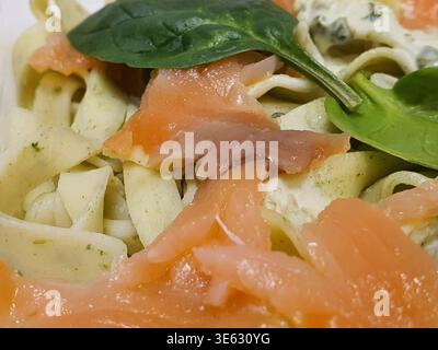 Makroaufnahme von frischen Tagliatelle- oder Fettuccinnudeln, belegt mit Räucherlachsscheiben und garniert mit frischem grünen Spinat oder Stockfoto