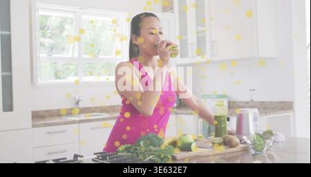 Trinkende Koreanerin, die grünen Smoothie in der Küche macht, mit einem magentafarbenen Tank und einem Mixbecher Stockfoto