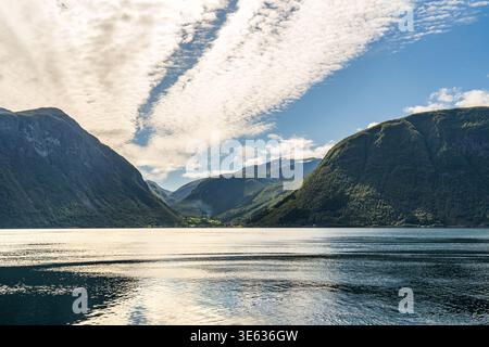 Majestätisches Panorama eines norwegischen Fjords mit majestätischen grünen Bergen, die in ruhiges, kristallklares Wasser tauchen. Der Himmel ist mit spektakulärem cl übersät Stockfoto