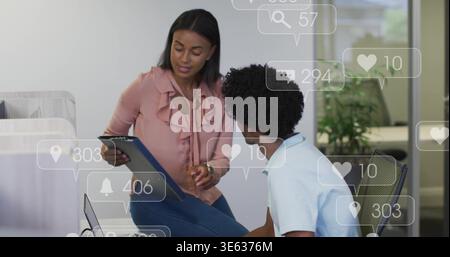 Frau mit Gesten aus rosafarbener Bluse, die den Ordner auf einen weißen Polomann im Büro zeigt, mit Laptop, Social Icons Stockfoto