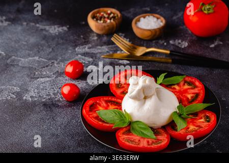 Caprese-Salat mit Tomaten, Burrata und Basilikum. Dunkler Hintergrund. Stockfoto