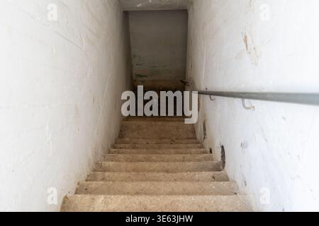 Ein Blick die Treppe hinunter, die in einen Betonbombenschutz in Israel führt. Der Unterstand verfügt über schlichte Wände und eine einfache Treppe. Die Umgebung ist umschlossen und zweckmäßig. Stockfoto