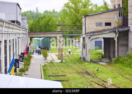 Ein Industrieeisenbahndepot oder eine Werkstatt während einer Open House-Veranstaltung, bei der Besucher auf einem asphaltierten Pfad neben nummerierten weißen Industrieanlagen spazieren gehen Stockfoto