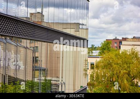Modernes, modernes Gebäude mit reflektierender Glasfassade, die die städtischen Strukturen und den bewölkten Himmel widerspiegelt. Die Architektur zeigt ein Stockfoto