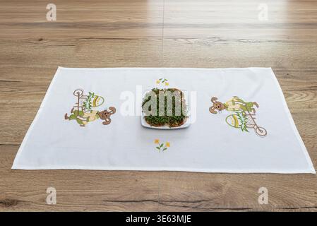 Grüne Kresse, die auf einem weißen Teller wachsen, auf einem gestickten ostertischläufer platziert Stockfoto