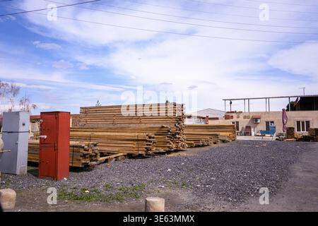 Holzstapel liegen baubereit auf Schotterboden. Rote Aufbewahrungsbox und grauer Versorgungsschrank stehen in der Nähe. Blauer Himmel mit weißen Wolken über ihm Stockfoto