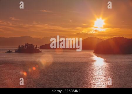 Der Sonnenuntergang am goldenen Alaska-Fjord beleuchtet das ruhige Wasser und die Silhouetten der Wälder Stockfoto