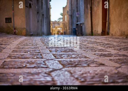 Ein flacher Blickwinkel aus der Nähe einer nassen Kopfsteinpflasterstraße in einer alten italienischen Stadt. Der alte Steinpflaster glitzert vor Feuchtigkeit und schafft Stockfoto