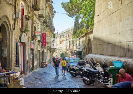 Eine enge Kopfsteinpflasterstraße im historischen Neapel, Italien, gesäumt von verwitterten alten Gebäuden mit Balkonen und Fensterläden. Mehrere Motoren Stockfoto