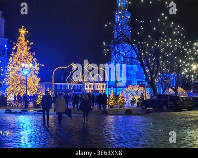 Eine nächtliche Szene eines europäischen Marktplatzes, der zu Weihnachten dekoriert ist, mit einem großen beleuchteten Weihnachtsbaum mit goldenen Lichtern und einem Stern Stockfoto