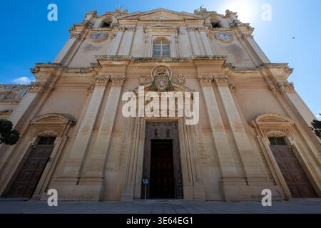 Flacher Blick auf die barocke Kalksteinfassade und das Hauptportal der St. Paul's Cathedral in Mdina, Malta, mit Besuchern am Eingang unter einem klaren bl Stockfoto