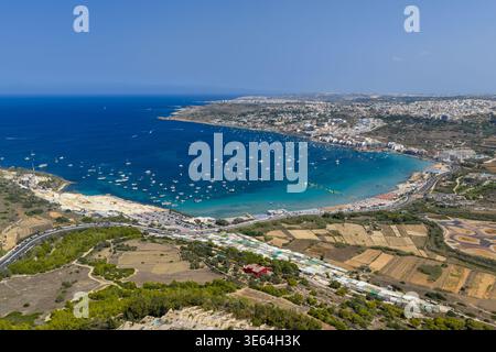 Aus der Vogelperspektive auf die Bucht von Ghadira und die Küste von Mellieha in Malta mit gekrümmtem Sandstrand, türkisfarbenem Wasser, Booten und Gebäuden am Hang unter klarer Summe Stockfoto
