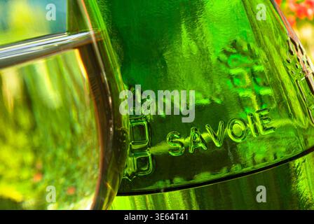 Weinflasche Savoie Jacquère und knackiges aromatisches Glas Wein aus nächster Nähe, mit grünem Glas geprägtem Schriftzug, im Garten mit natürlichem Sonnenlicht in Ostfrankreich Stockfoto