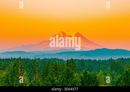 Der legendäre Mount Rainier ist in intensiven orange- und rosa Sonnenuntergangsfarben getaucht und hat mehrschichtige Grate im Vordergrund. Stockfoto