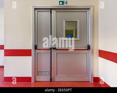 Notausgangstür mit Schiebegriffen an weißer Wand mit roten Streifen - Feuerausgangsymbol über der Tür eines öffentlichen Gebäudes sichtbar Stockfoto