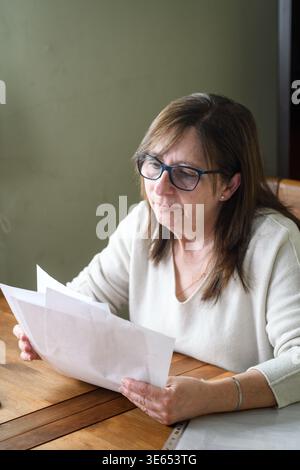Senior Frau, die Dokumente am Schreibtisch überprüft Stockfoto