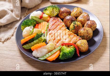 Teller mit gegrilltem Huhn mit gedämpftem Gemüse und gebackenen Kartoffeln auf Holztisch Stockfoto