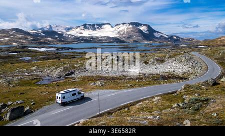 Ein weißer Wohnmobil rastet entlang der Straße 55 auf dem Sognefjellet-Plateau. Der Blick aus der Vogelperspektive fängt den Asphalt ein, der sich durch alpine Seen und Tundra schlängelt Stockfoto