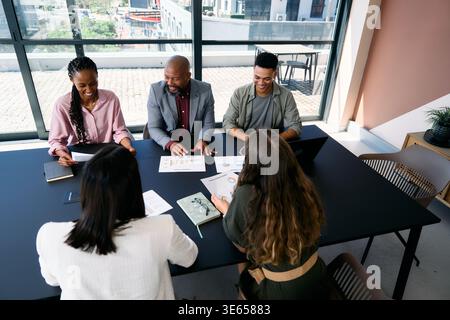 Lächelndes Team von Fachleuten, die tagsüber im Konferenzraum im Büro über Business Charts diskutieren Stockfoto