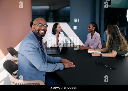 Lächelnder, reifer Geschäftsmann mit Kollegen während der Besprechung tagsüber im Sitzungssaal im Büro Stockfoto