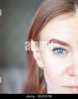 Nahaufnahme eines Porträts einer jungen Frau mit blauen Augen und rotem Haar, das gepflegte Augenbrauen und natürliches Make-up vor einem verschwommenen Hintergrund zeigt Stockfoto
