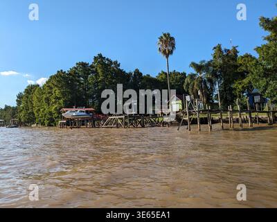 Farbenfrohe Pfahlhäuser und hölzerne Docks säumen das üppig grüne Flussufer des Parana-Deltas in Tigre, Argentinien. Blauer Himmel. Stockfoto