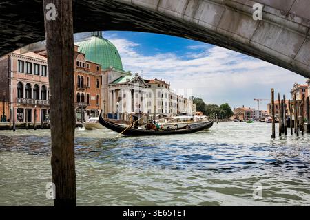 Blick unter einer venezianischen Brücke mit Gondeln auf dem Kanal, eingerahmt von historischen Gebäuden und einer Kuppelkirche in der Ferne Stockfoto