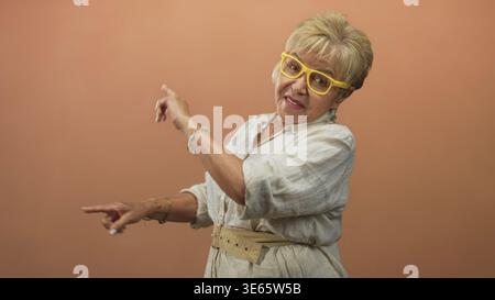 Die ranghanische Frau zeigt Zeigefinger und Gesten, trägt gelbe Brille, türkisfarbene Armbänder und einen Gürtel im Studio; fröhlich. Stockfoto
