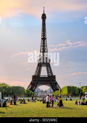 Paris, Frankreich - 08 05 2025: Eine vertikale Landschaft des berühmten Eiffelturms unter einem weichen Sonnenuntergang. Im Vordergrund sind zahlreiche Personen Sitten zu sehen Stockfoto